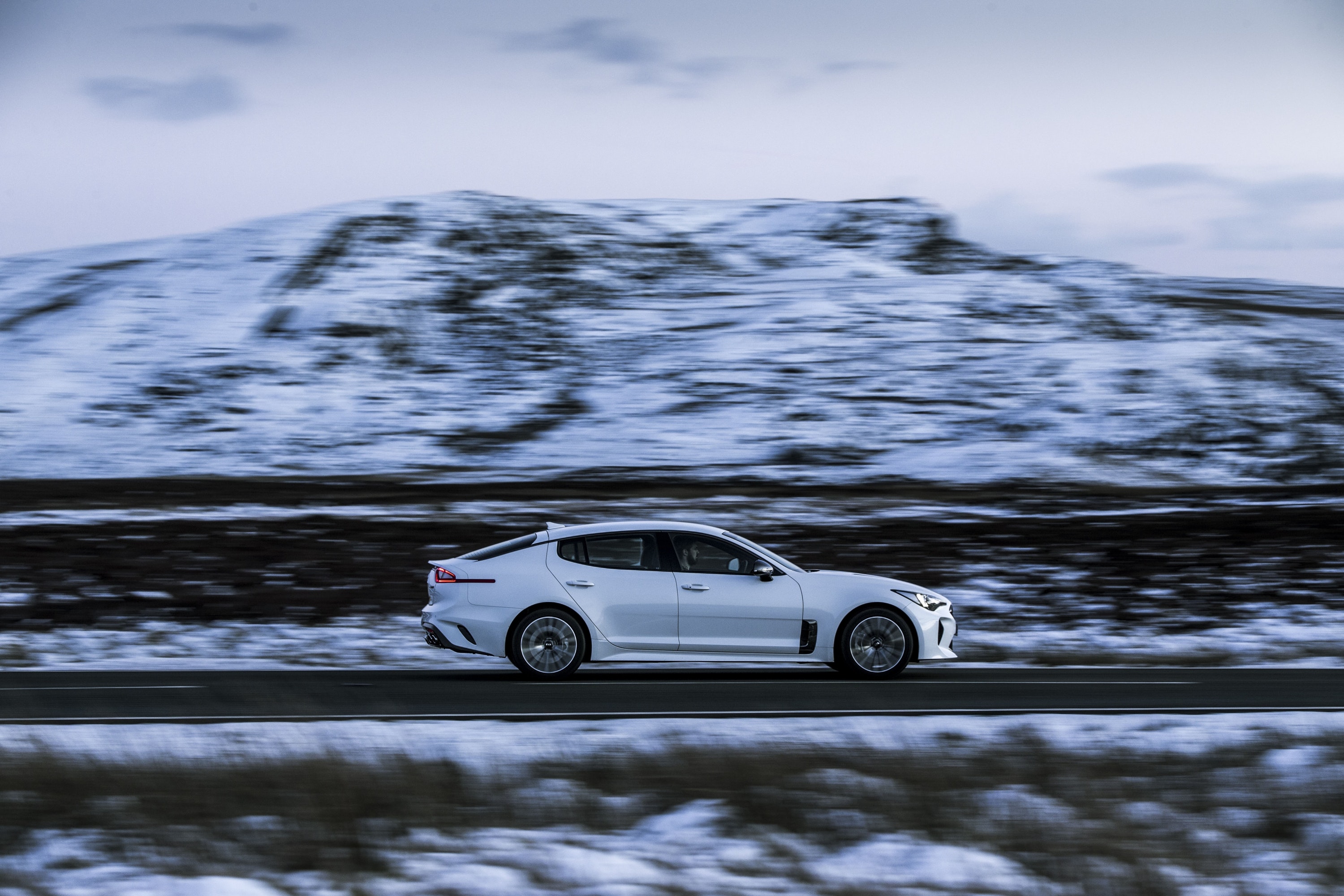 White Kia Stinger GT-Line driving on a road through snowy mountains